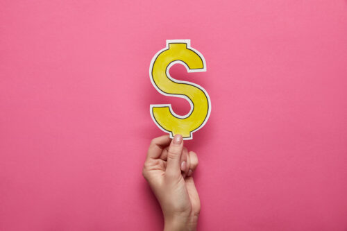 A hand holding a piece of paper in the shape of a dollar sign