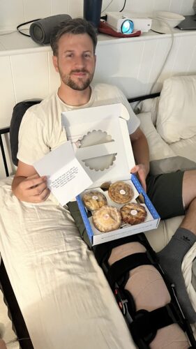 young man with a knee brace holding a care package of pies