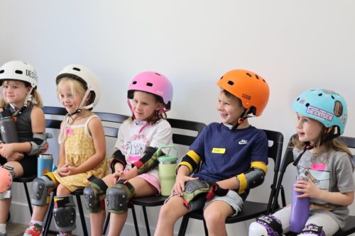 young children sit in a row in chairs with helmets on