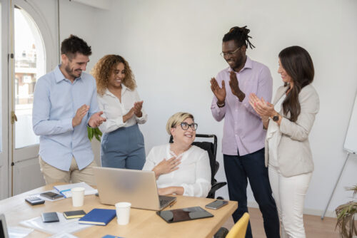 Coworkers standing around a fellow worker and clapping and smiling